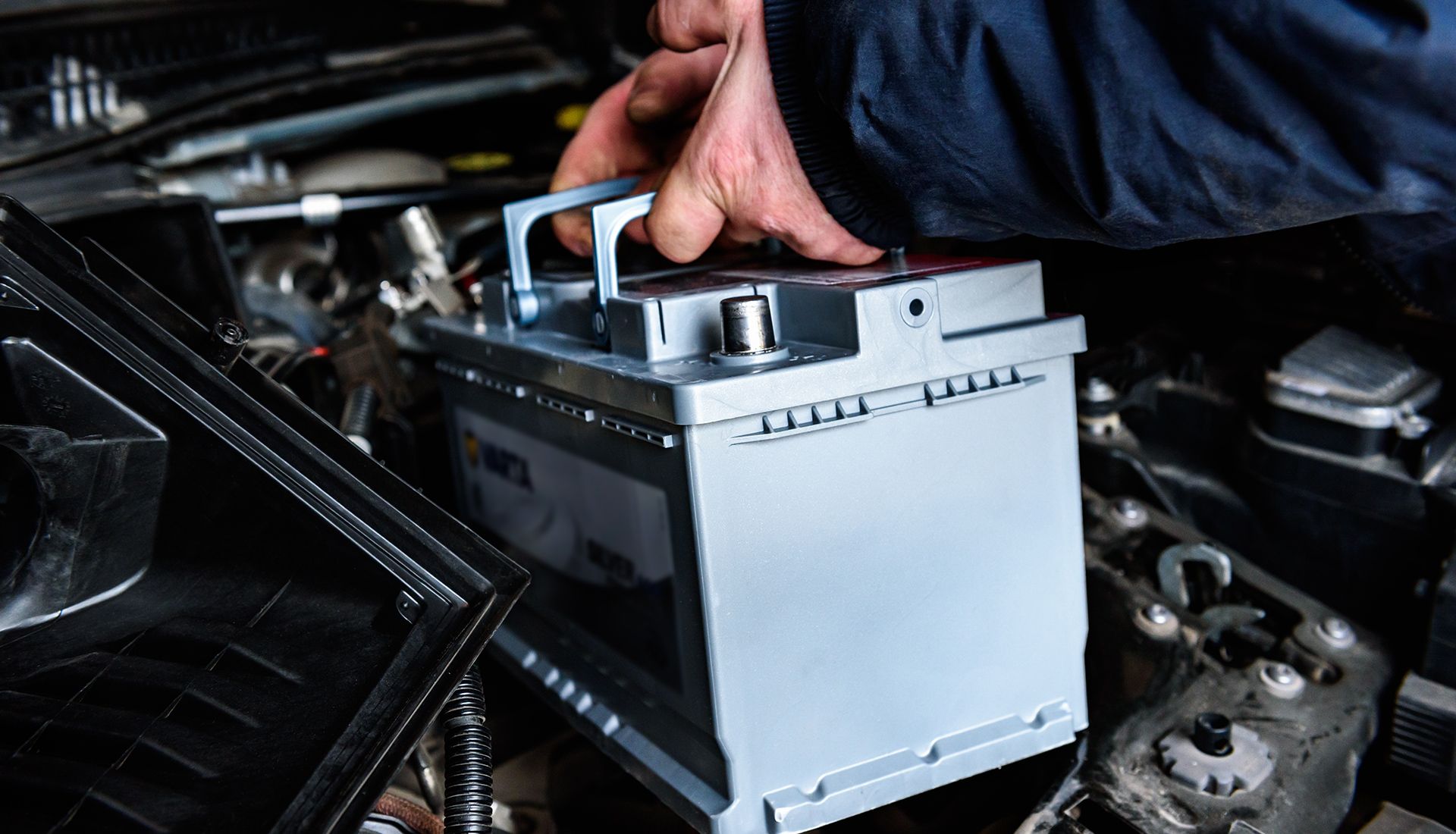 Hand lifting a car battery from engine compartment.