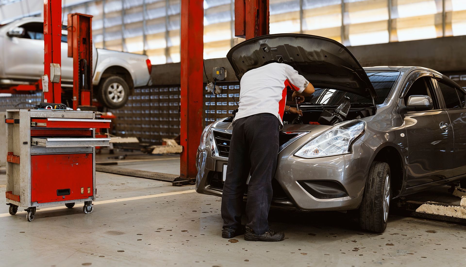 Mechanic working on car engine in a garage with red tool cabinet.