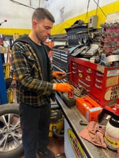 Mechanic smiling, holding tire and lug wrench, wearing overalls.