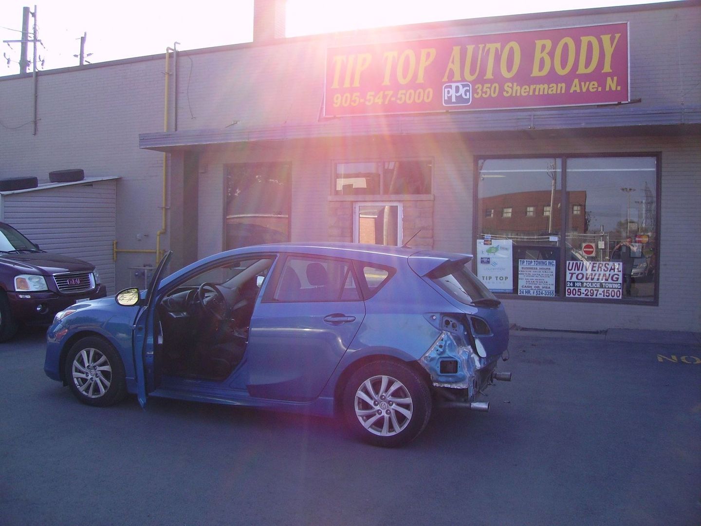 Small car with wrecked bumper parked in front of Tip Top Auto Body awaiting repairs