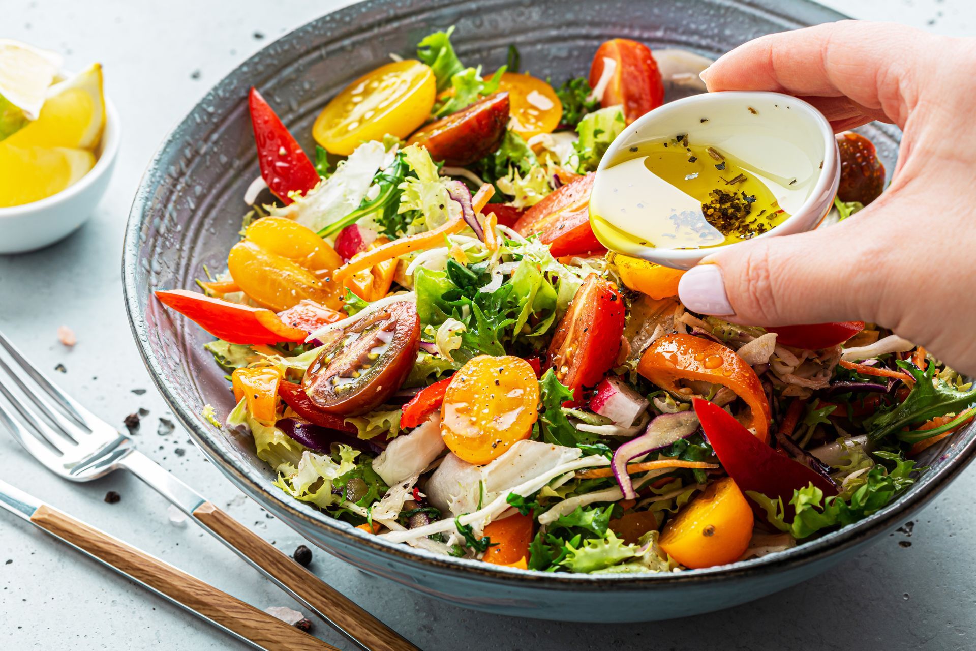 A person is pouring dressing on a salad in a bowl.