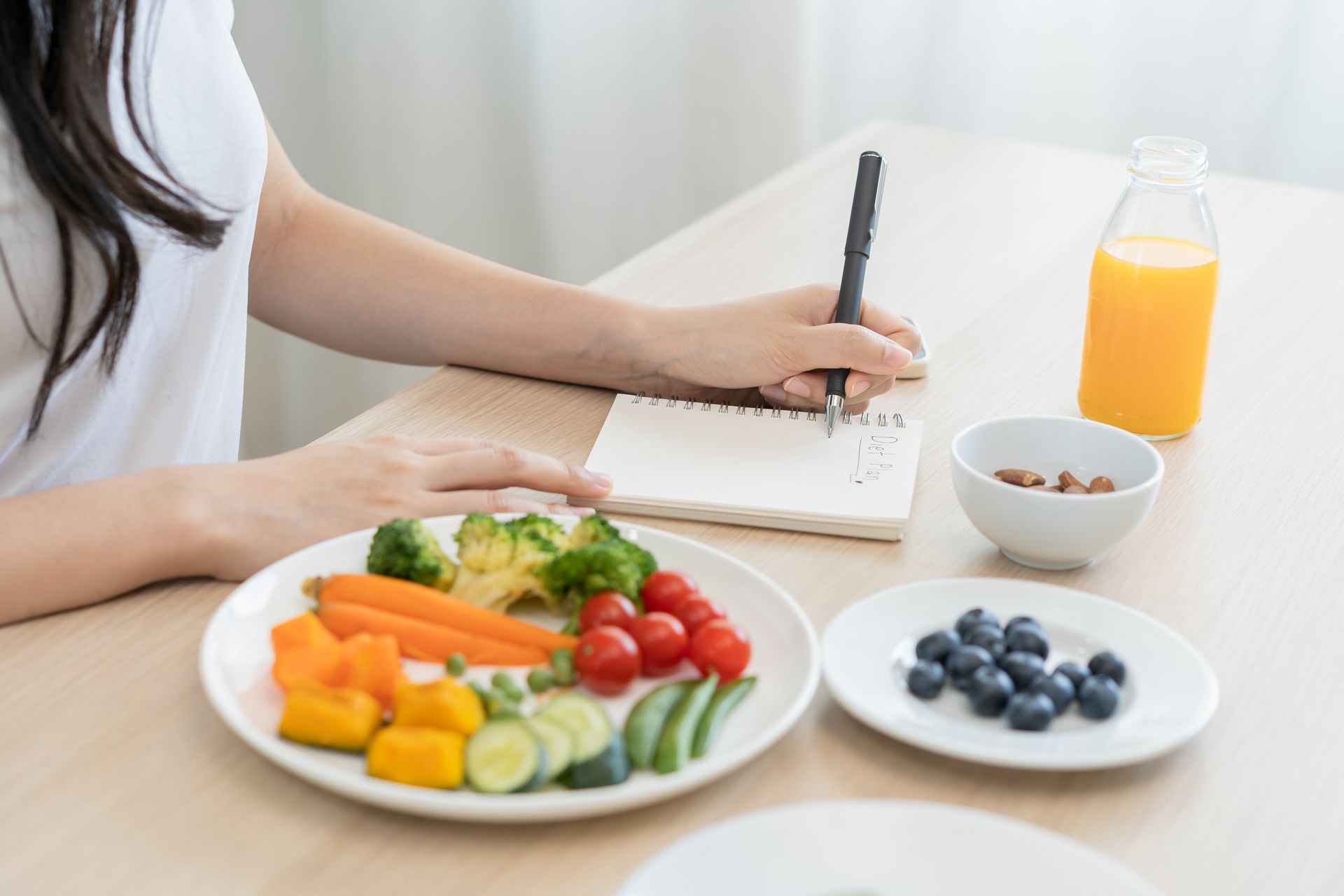 A woman is sitting at a table with a plate of vegetables and writing in a notebook.