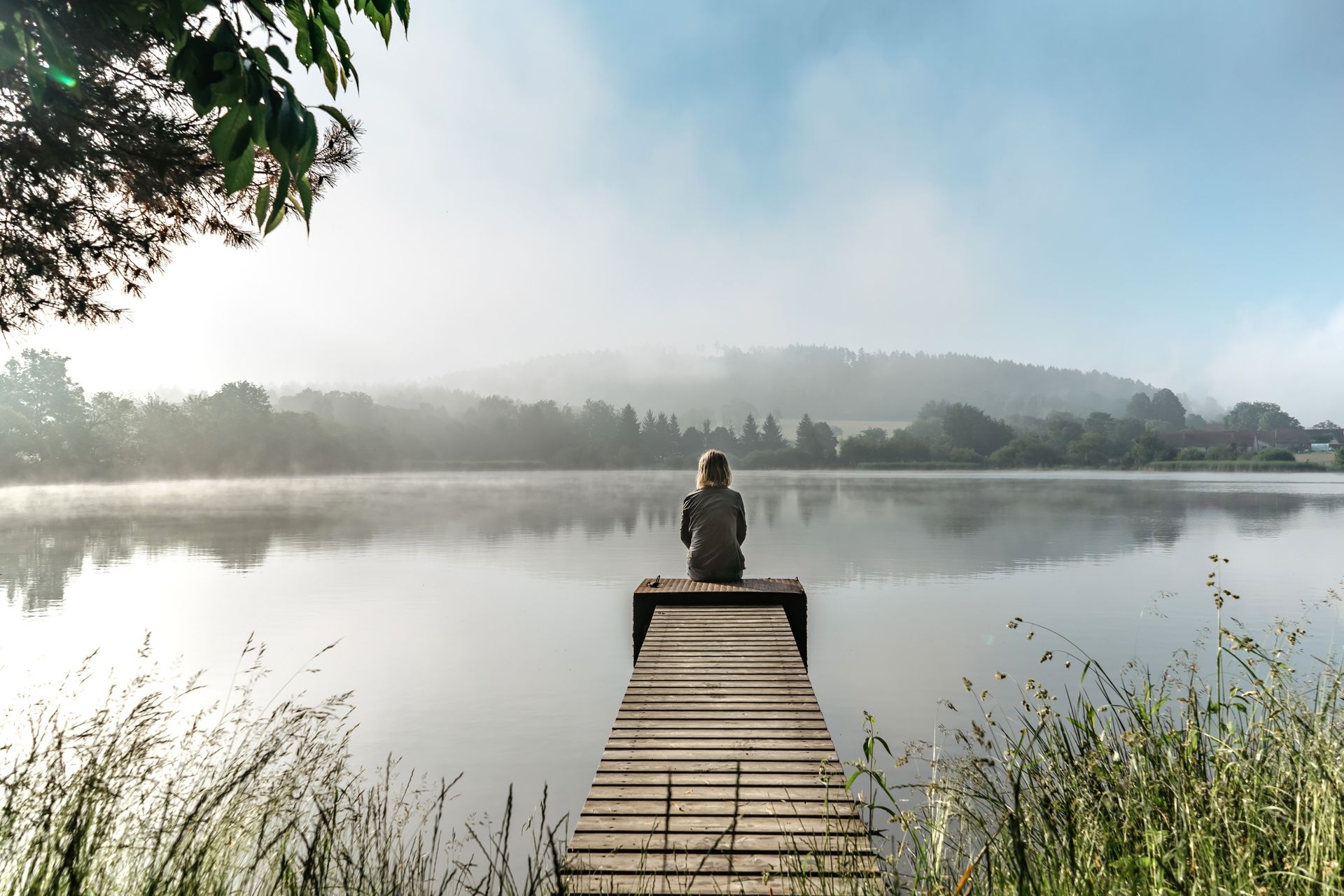 A person is sitting on a dock overlooking a lake.