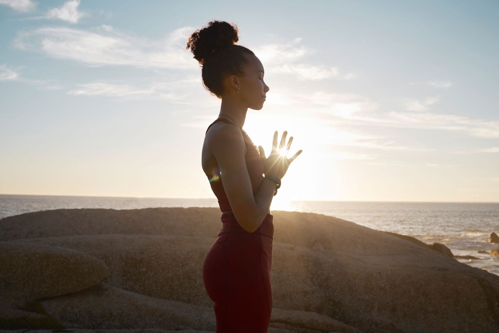A woman is practicing yoga on a rock near the ocean at sunset.
