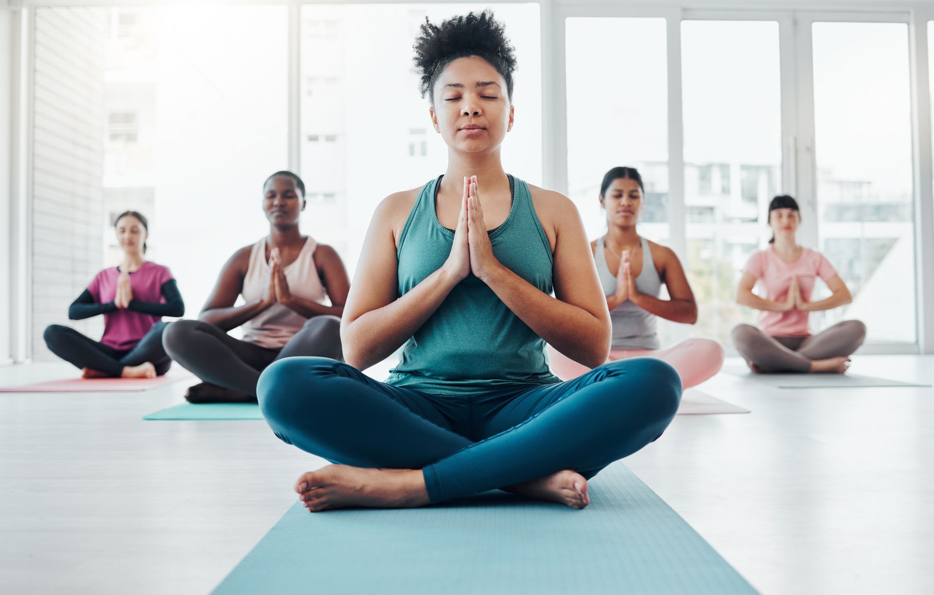 A group of women are sitting in a lotus position on yoga mats in a yoga studio.
