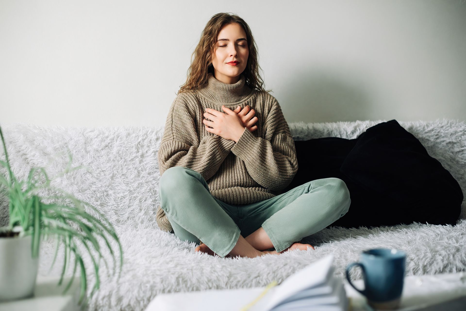 A woman is sitting on a couch with her legs crossed and her hands on her chest.