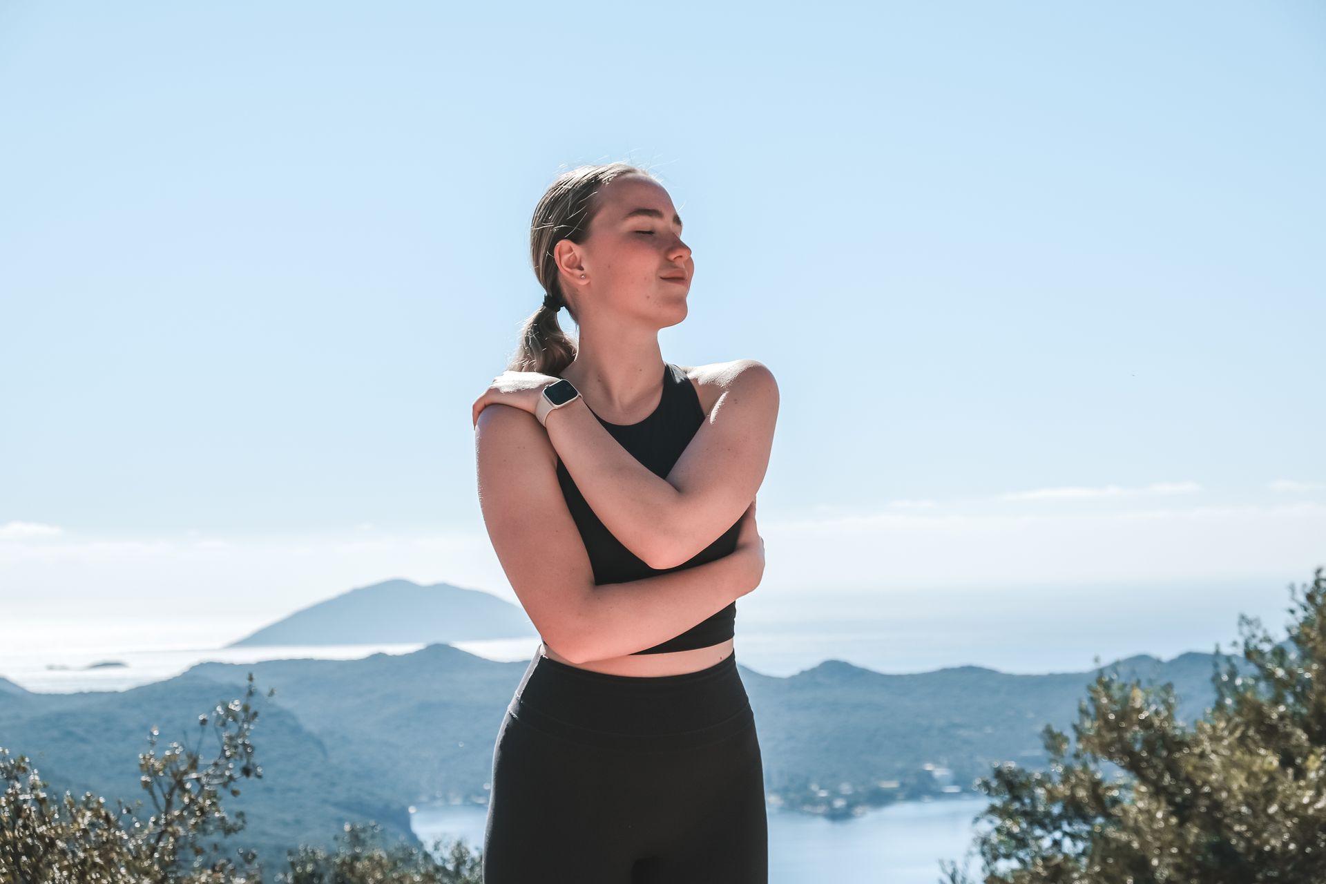 A woman is standing on top of a mountain with her arms crossed.