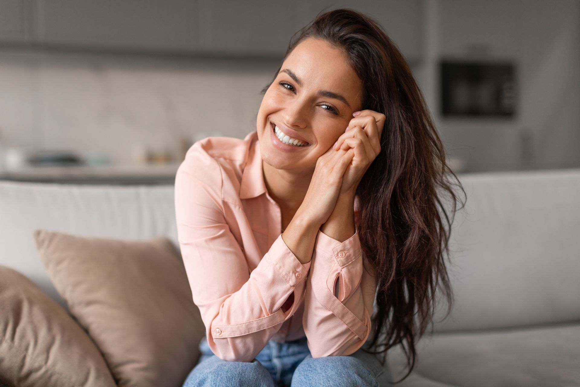 A woman is sitting on a couch with her legs crossed and smiling.