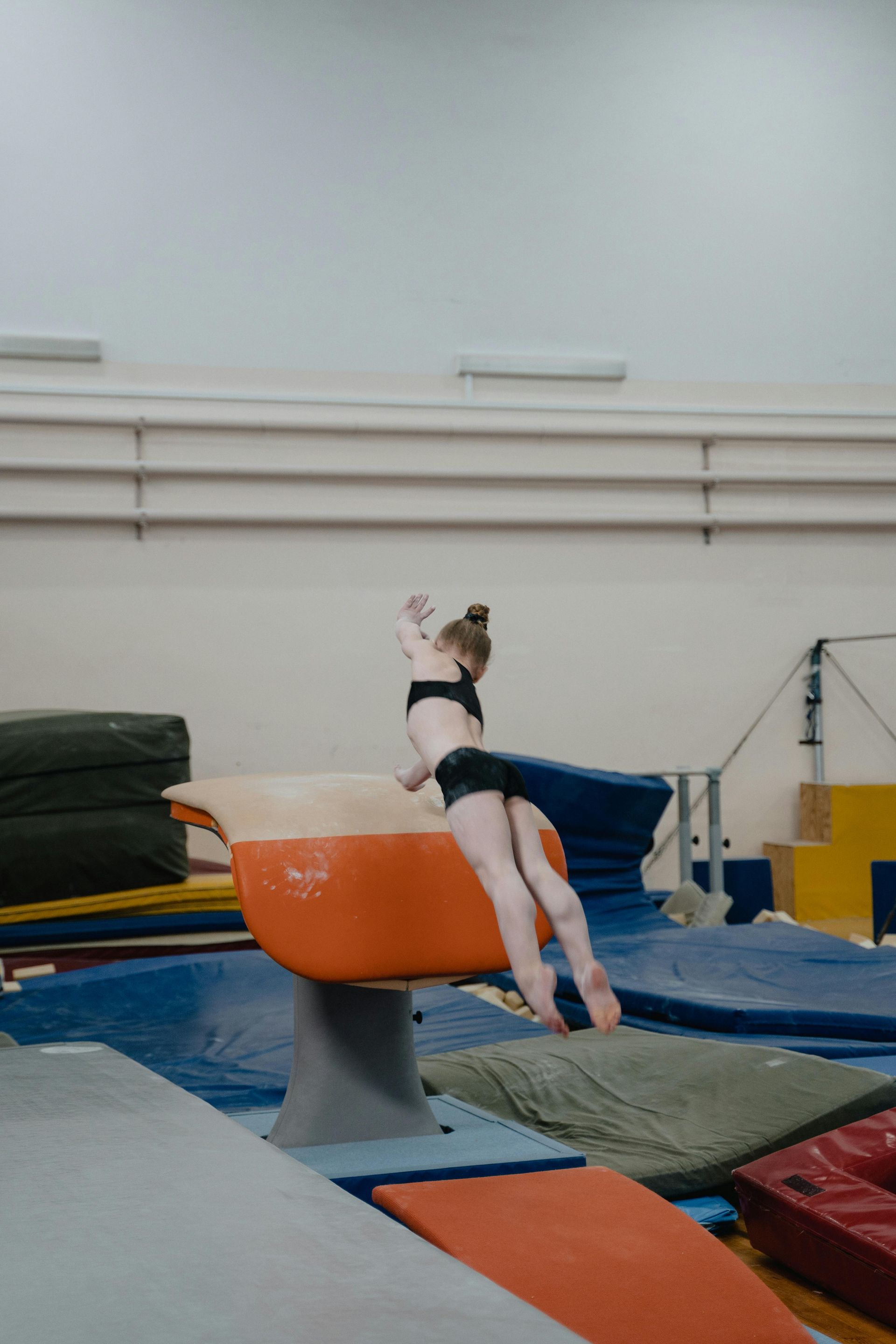 Gymnast performing a vault over an orange apparatus in a gym.