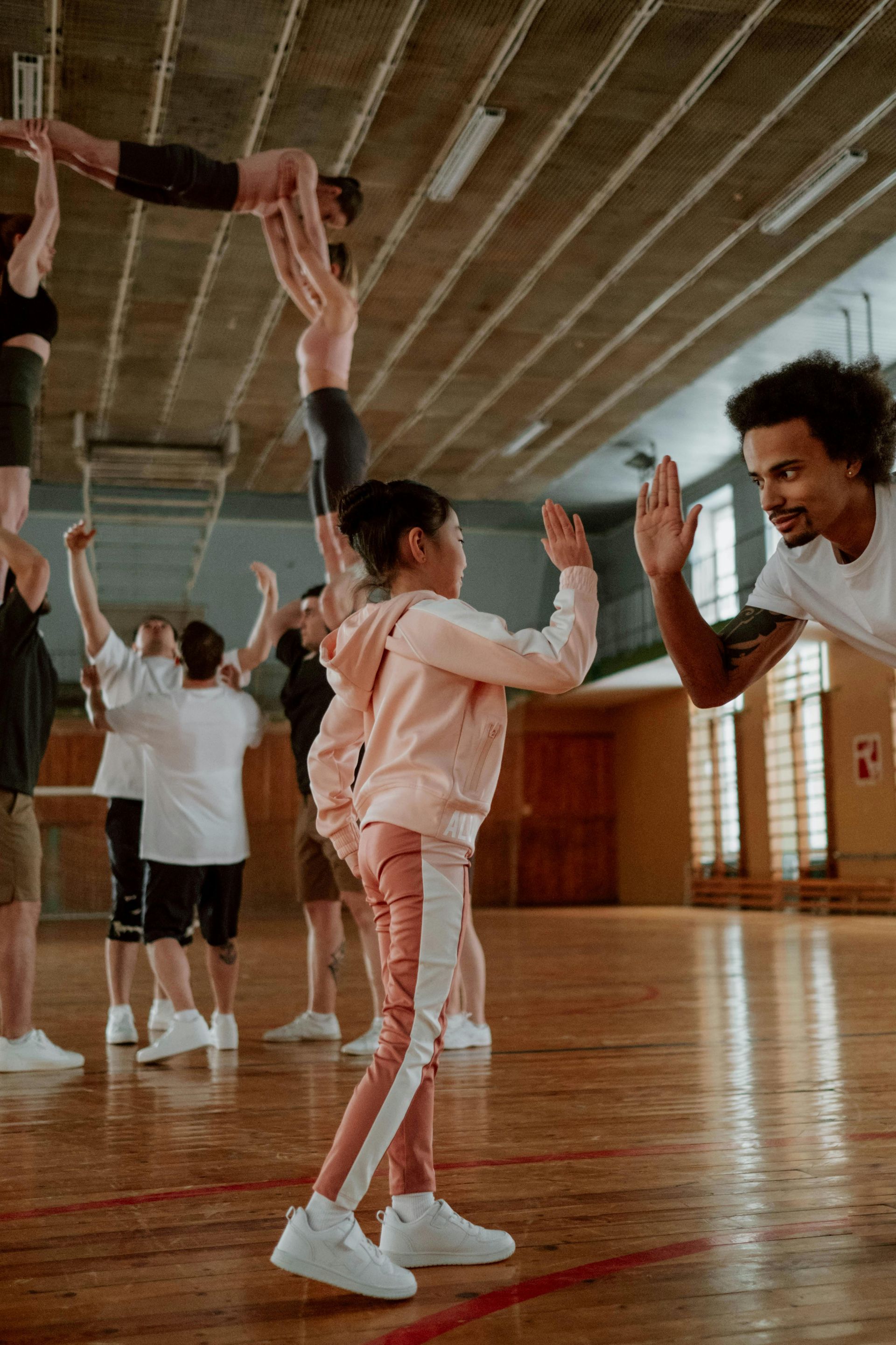 Gymnasium, acrobatic human pyramid. Child high-fives man. Others watch and support.