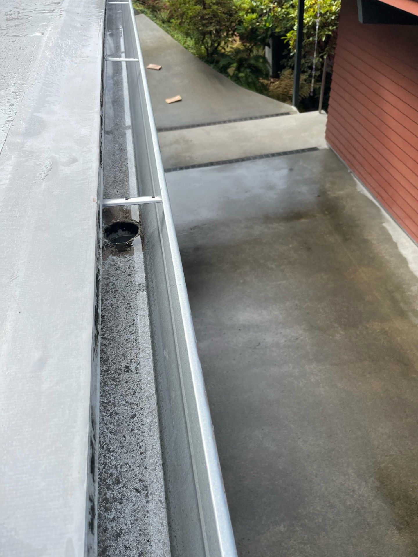 A drain on the side of a building next to a walkway