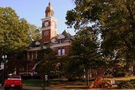 Brick courthouse with clock tower, surrounded by trees, red truck in foreground.