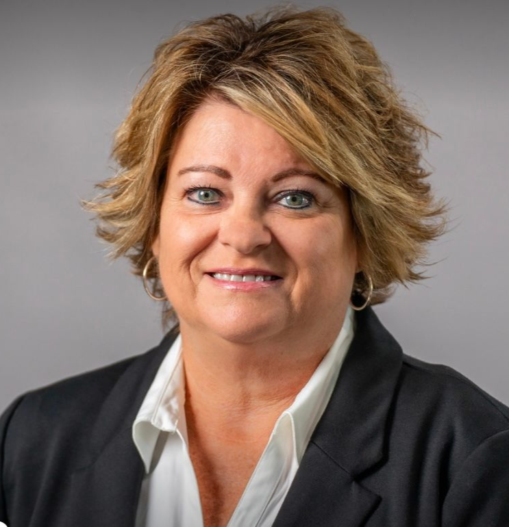 Woman in a black suit and white shirt smiles at the camera, against a grey background.