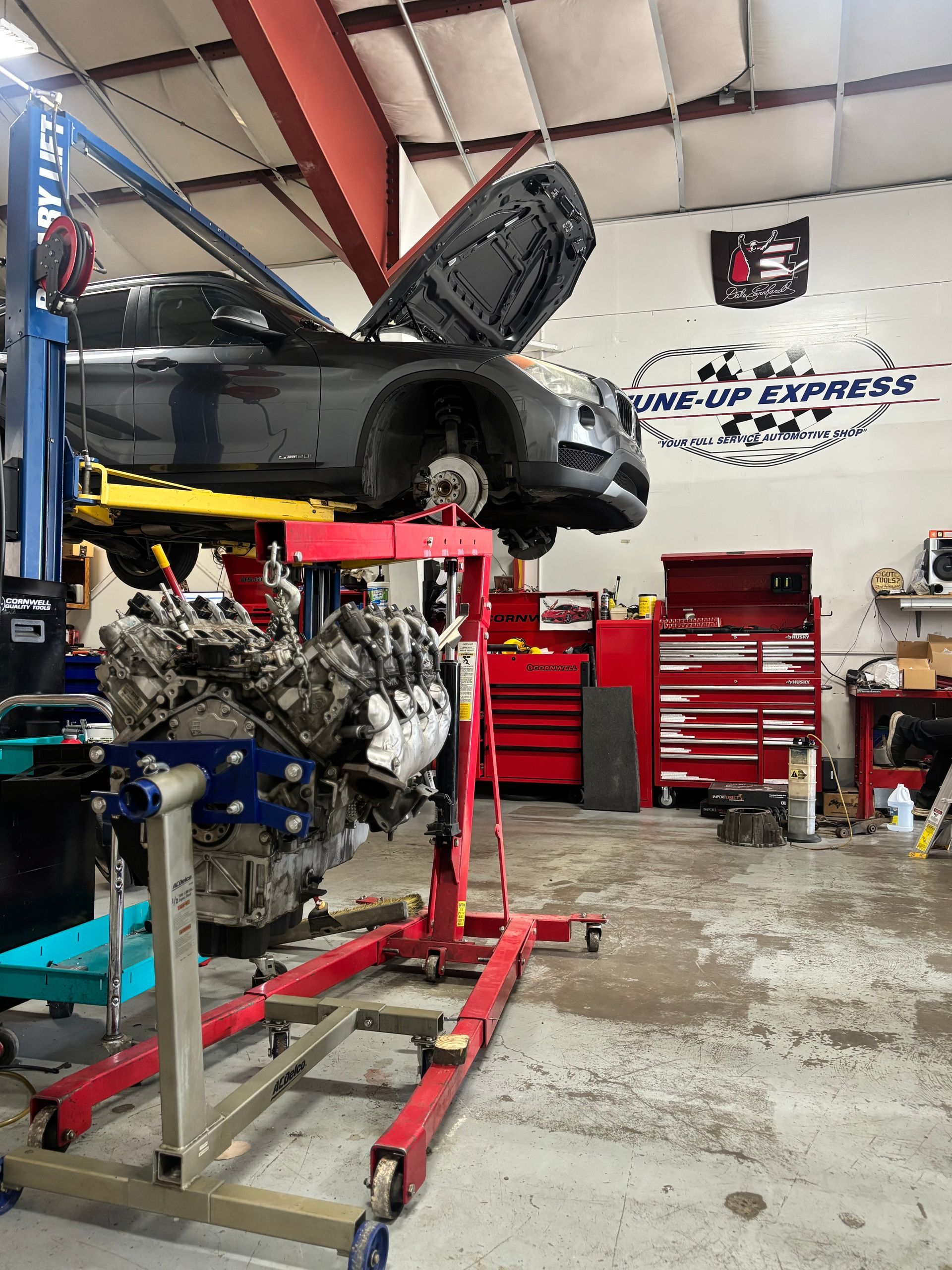 Black race car on lift in auto shop, engine exposed, red tool cabinets in background | Tune-Up Express Auto