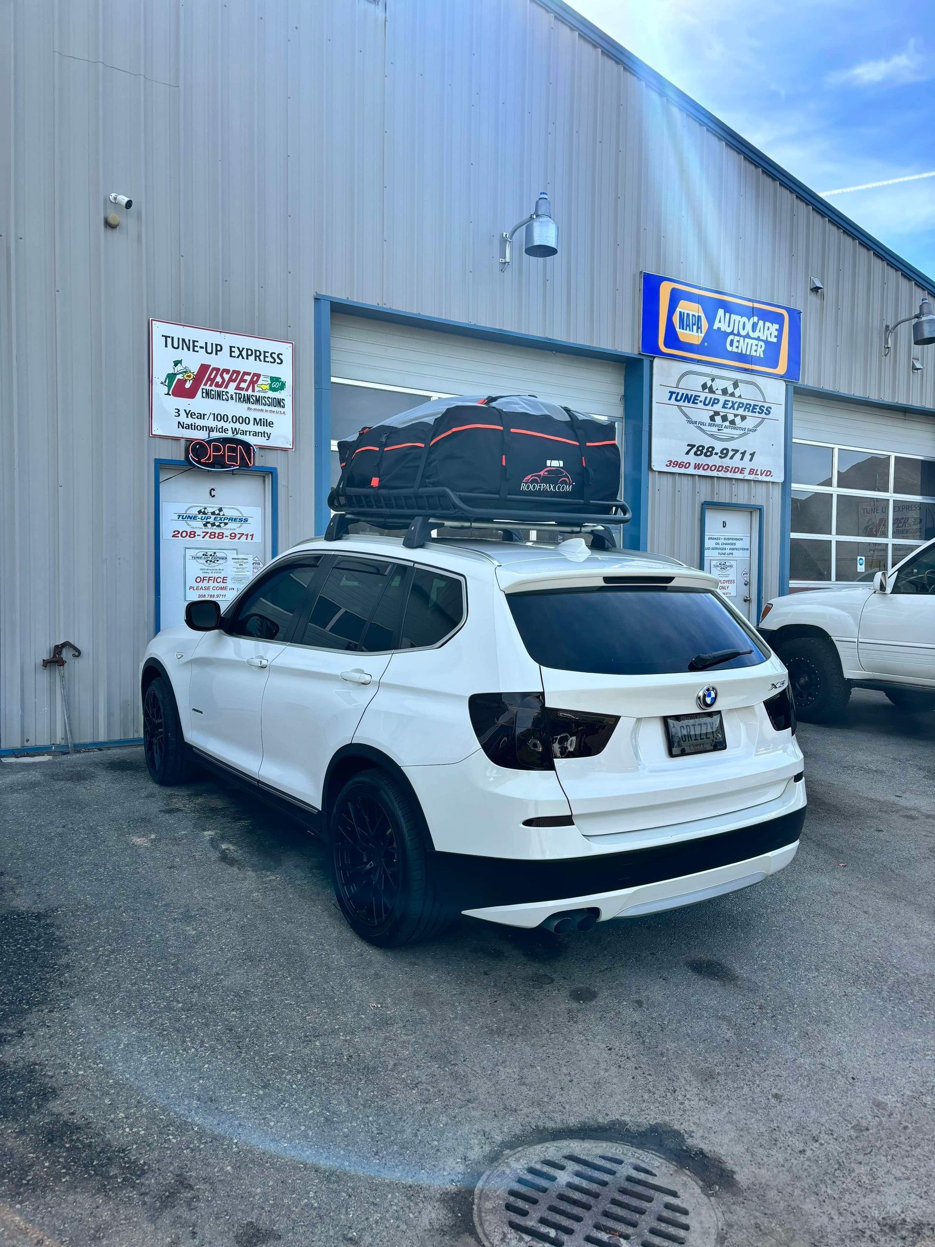 White SUV parked outside an auto repair shop with signs on a metal building. | Tune-Up Express Auto