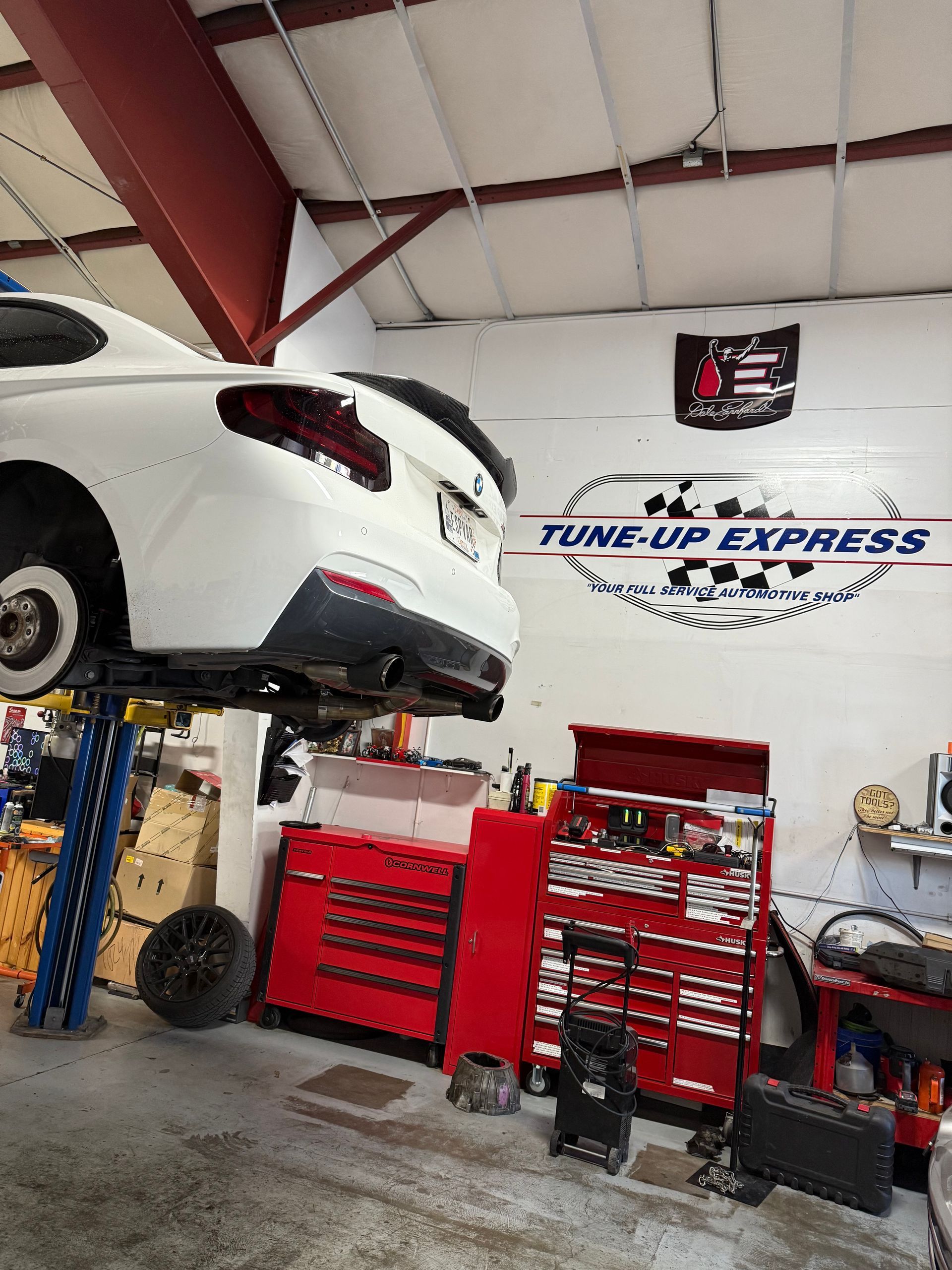 White sports car lifted in an auto repair shop with red tool cabinets and a Tune-Up Express sign. | Tune-Up Express Auto