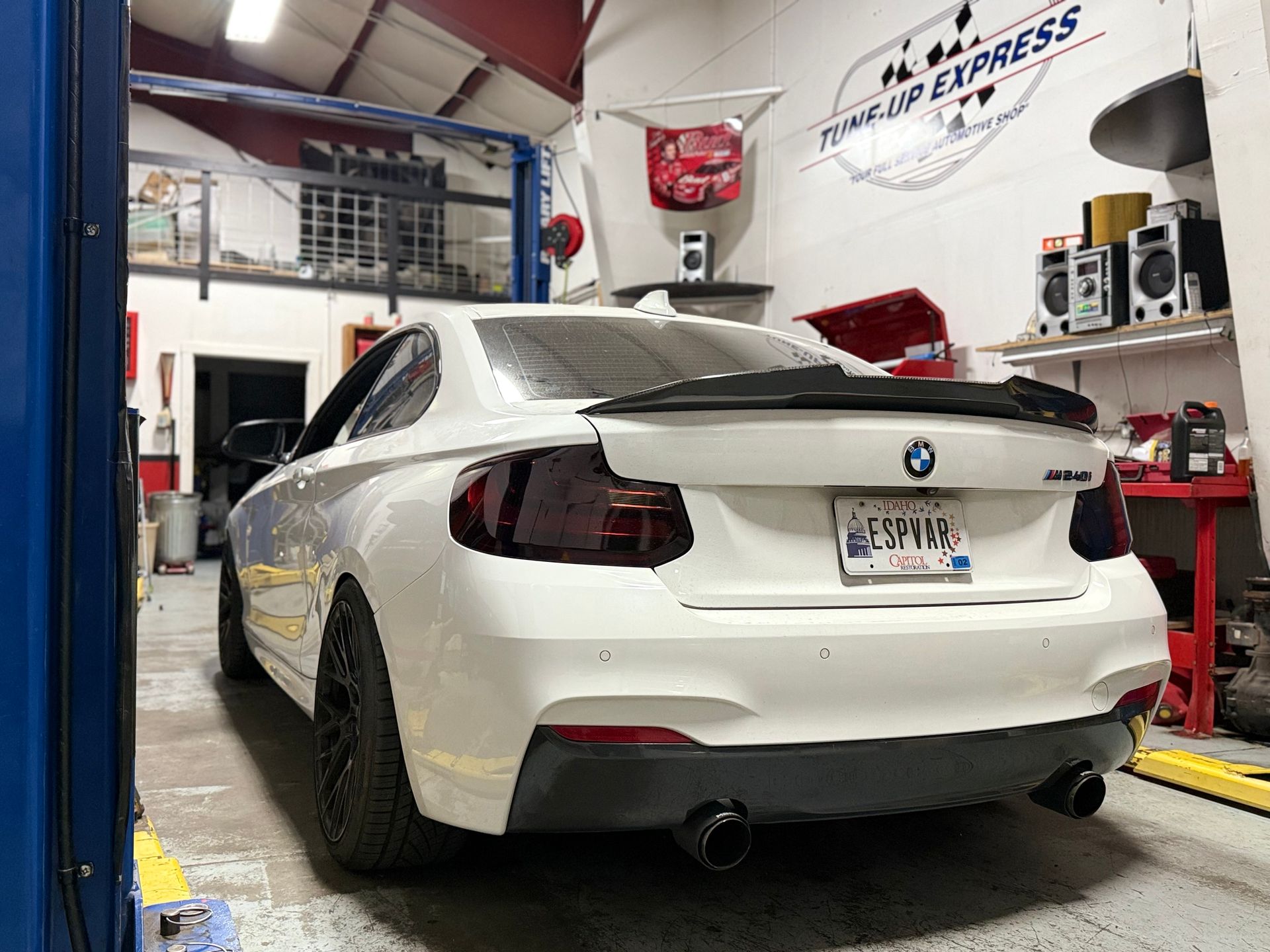 White BMW coupe in an auto shop, rear view, with red lift and tools around it | Tune-Up Express Auto