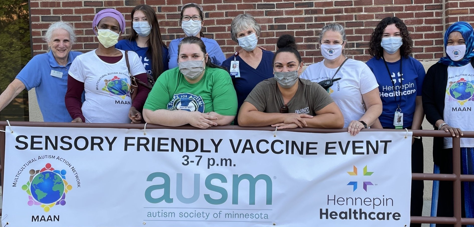 A group of people wearing masks are standing in front of a banner that says sensory friendly vaccine event.