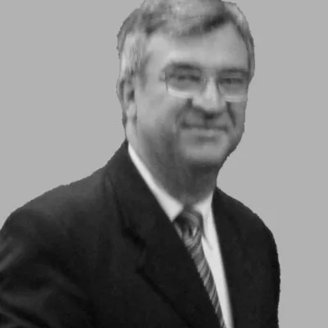 Hombre con traje y corbata, gafas y sonriendo ligeramente.