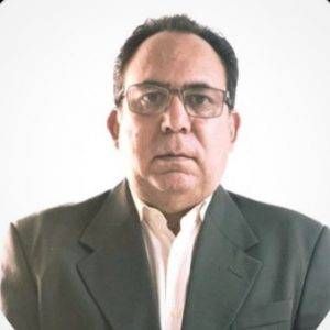 Hombre con gafas, traje y camisa blanca. Mira al frente.