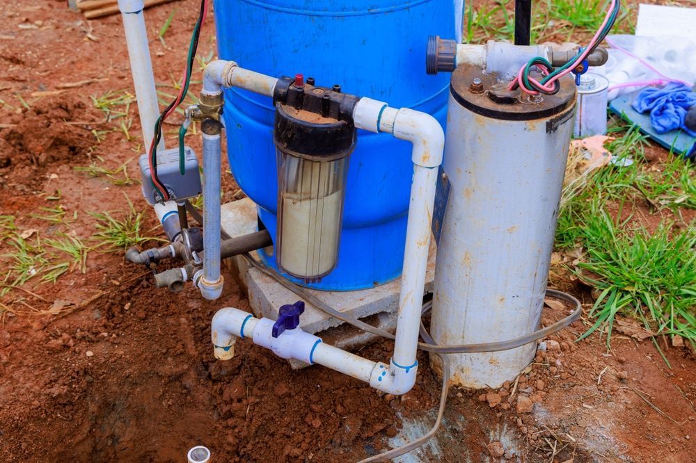 Well water filtration system with blue tank and white pipes. Filter is encased in a clear container.