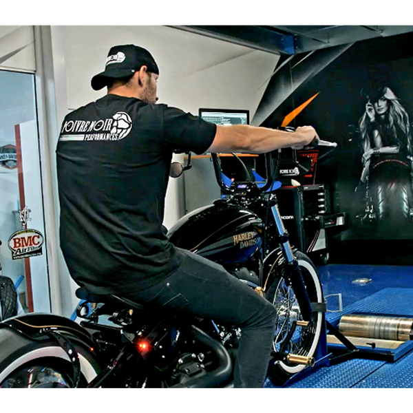 Un homme sur une moto noire dans un magasin, portant une chemise et une casquette noires,