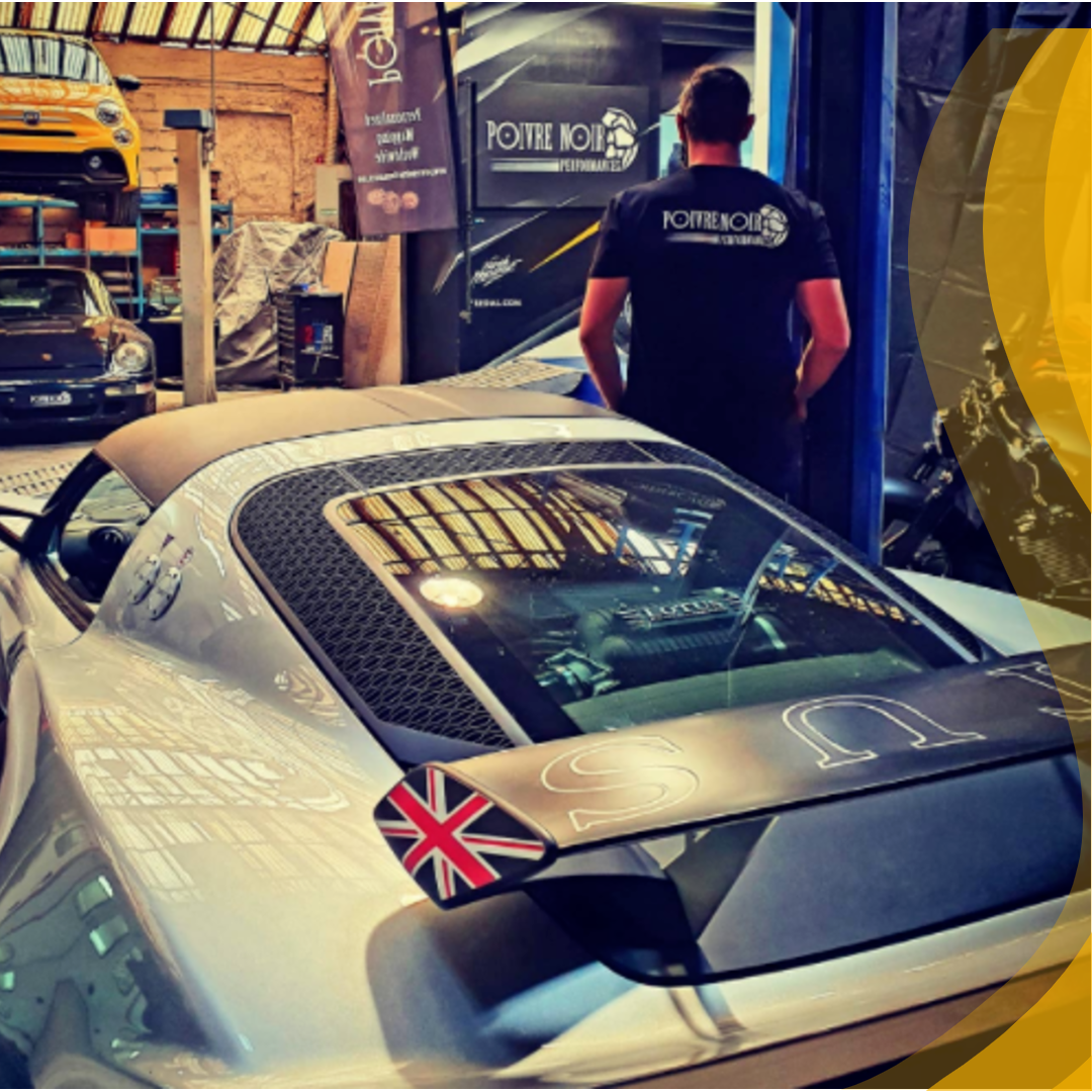 Voiture de sport argentée avec une aile de drapeau britannique, homme dans un garage.