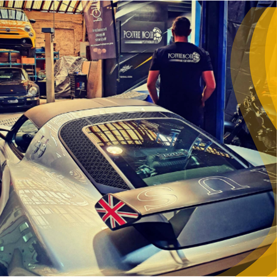 Voiture de sport argentée avec une aile de drapeau britannique, homme dans un garage.