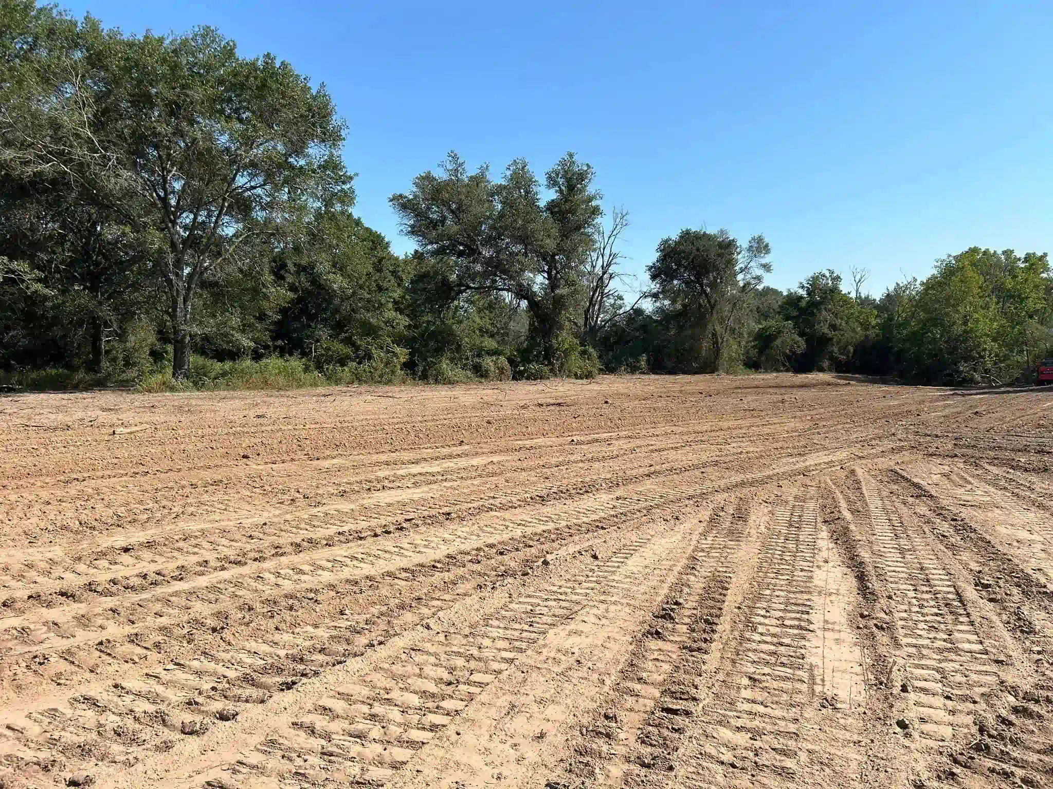 A dirt field with trees in the background and a blue sky
