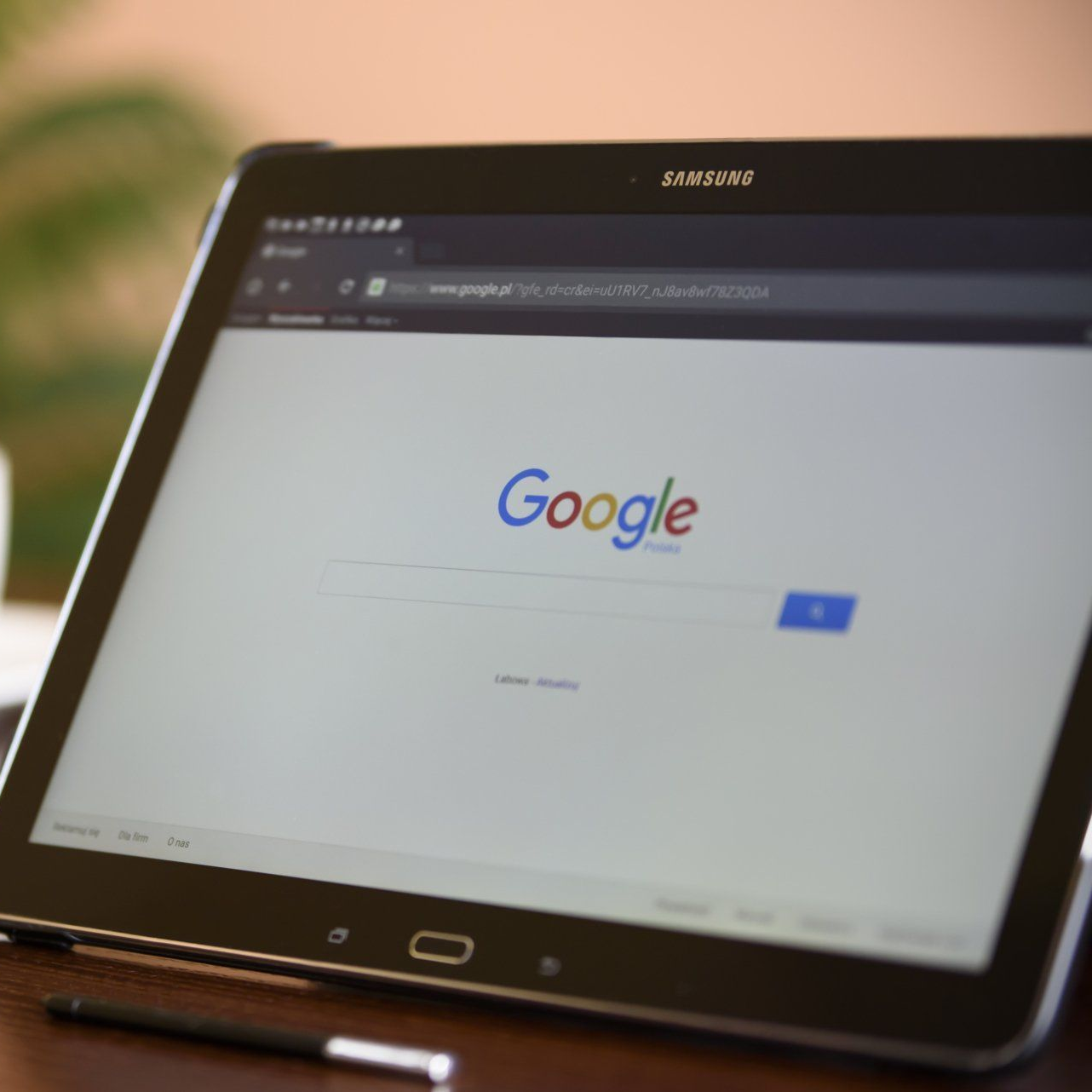 Tablet displaying Google search page. Black tablet, stylus on a table.