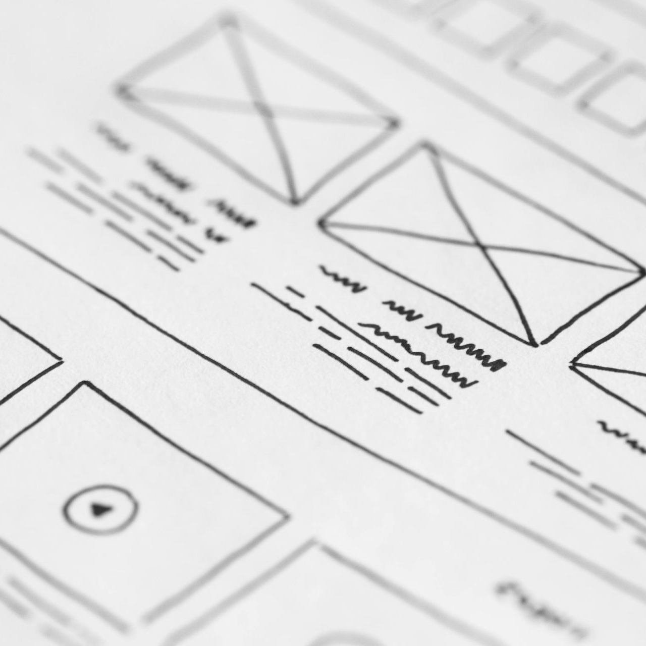Website wireframe sketch with boxes, lines, and placeholder text on white paper.