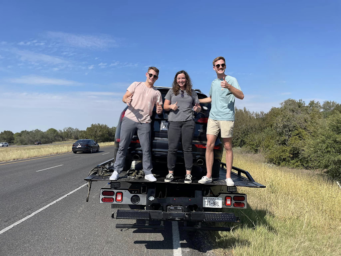 Three people are standing on the back of a truck.