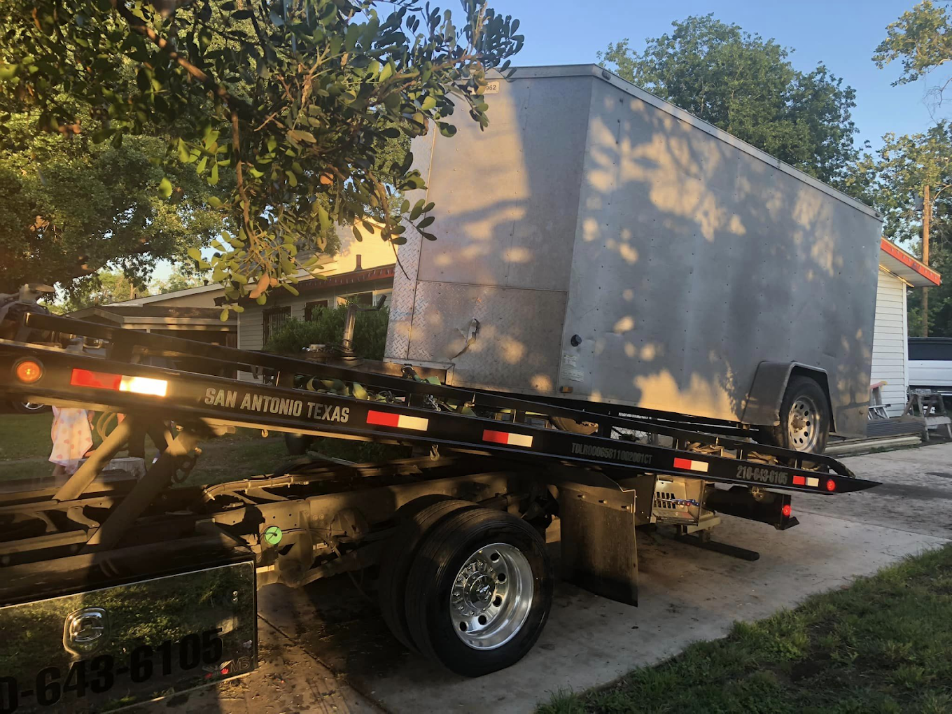 A tow truck with a trailer attached to it is parked in front of a house.