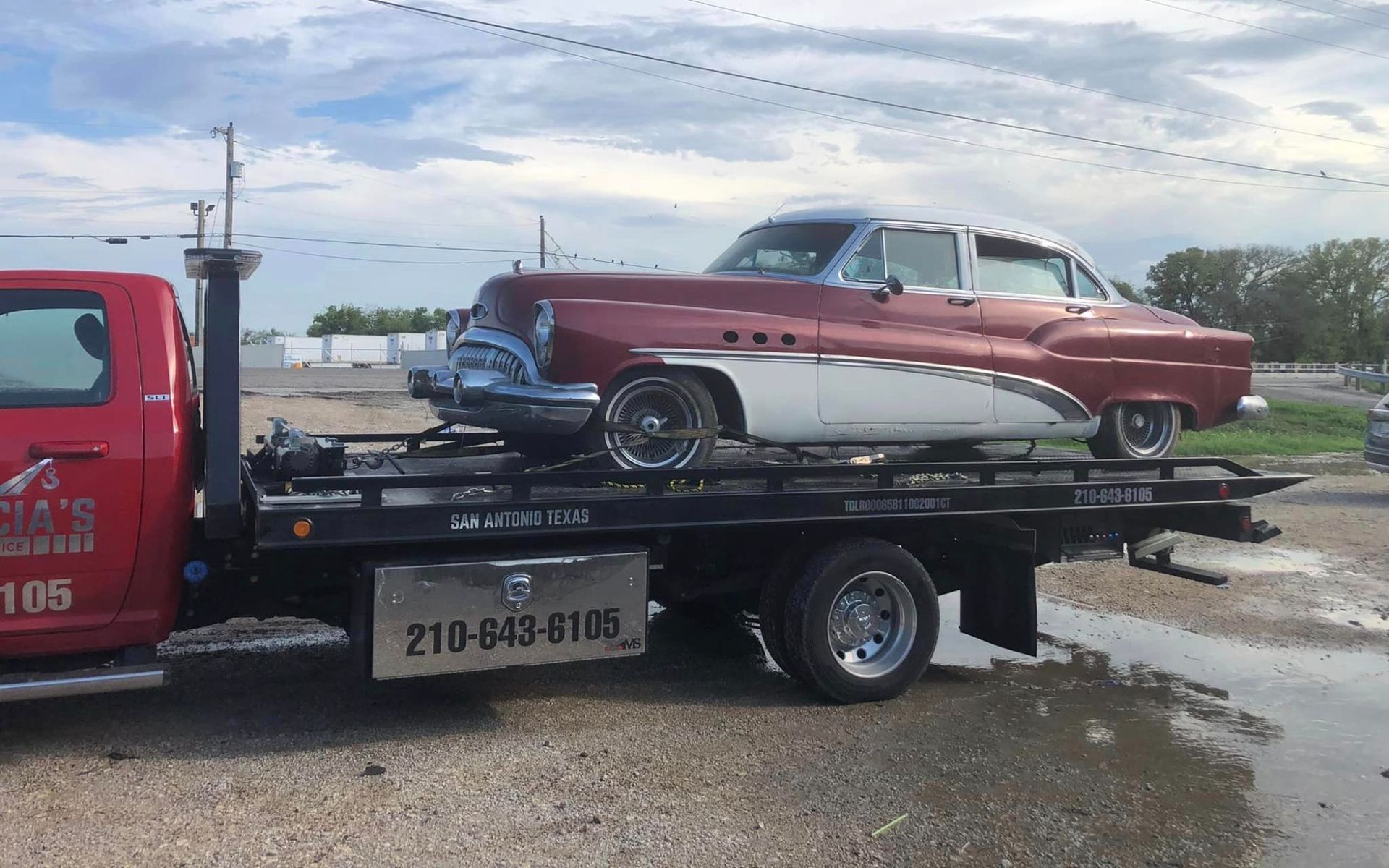 A red and white car is being towed by a tow truck