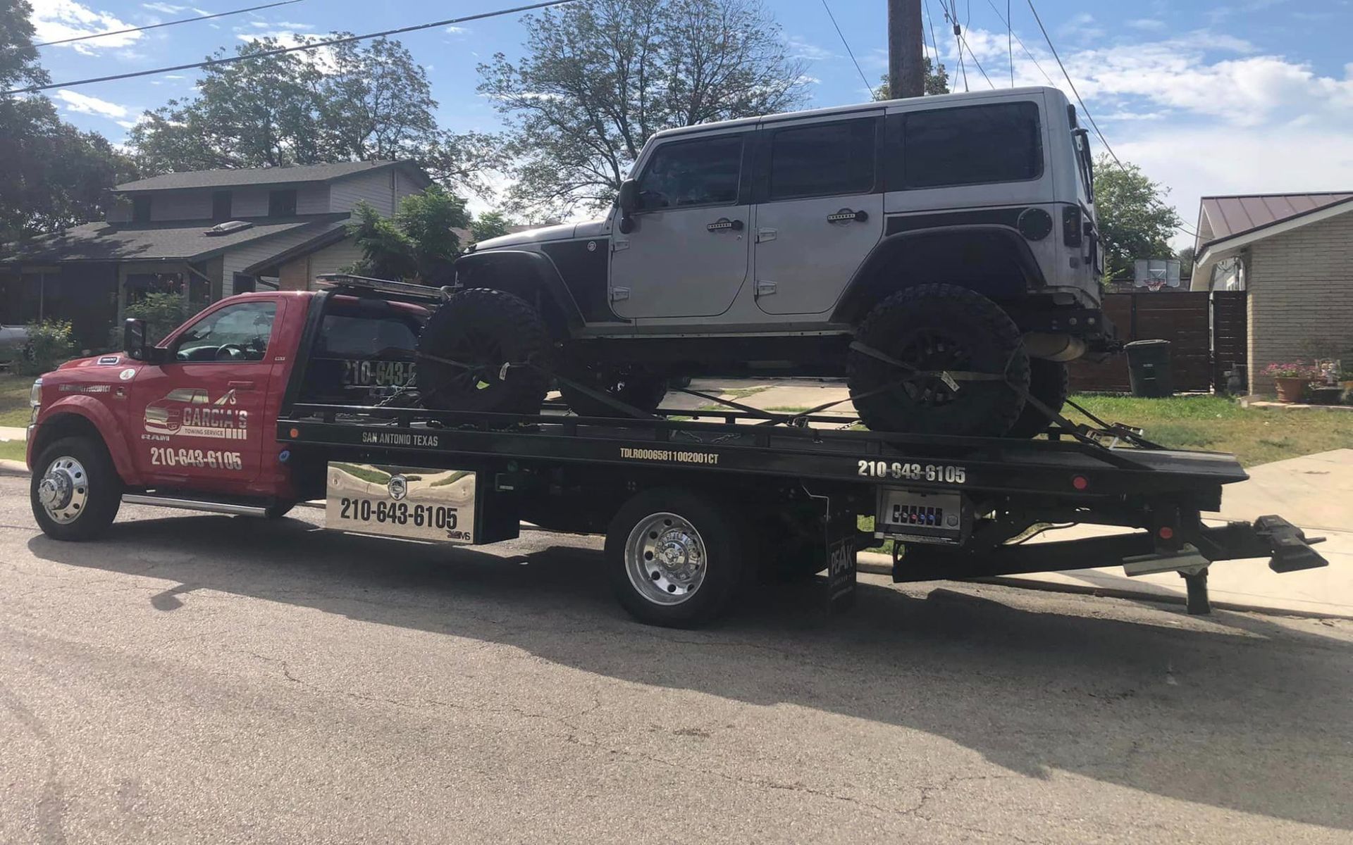 A tow truck is towing a jeep down a street.