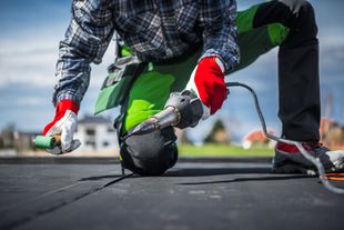 A man is kneeling down on a roof using a tool.