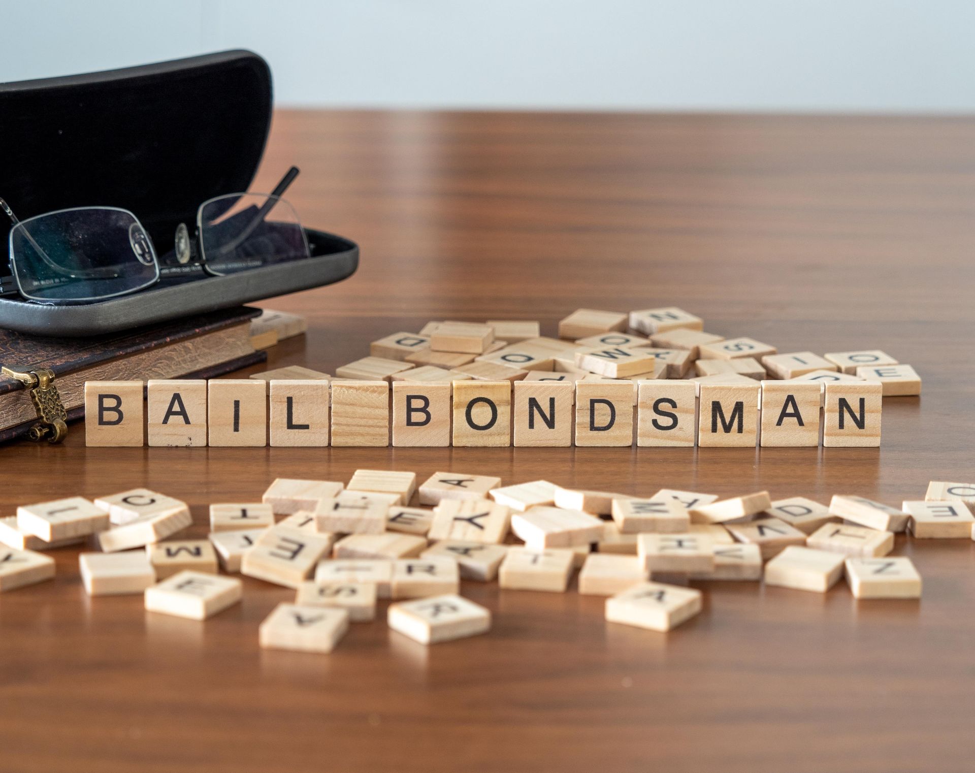 Wooden letter tiles spelling bail bondsman on a desk beside glasses and legal books.