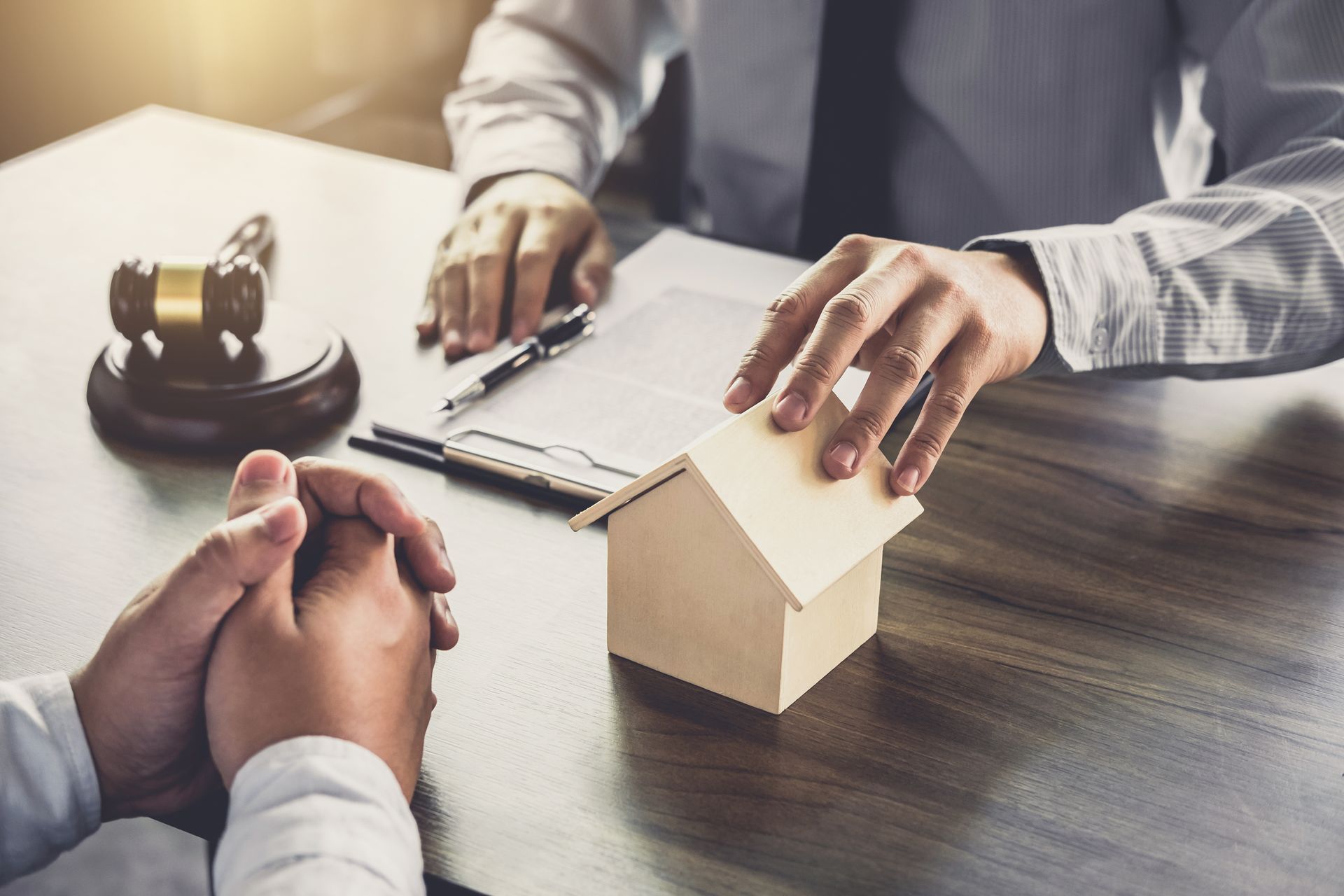 Person hands wooden house to another, legal document on table, gavel, interior shot Person hands wooden house to another, legal document on table, gavel, interior shot