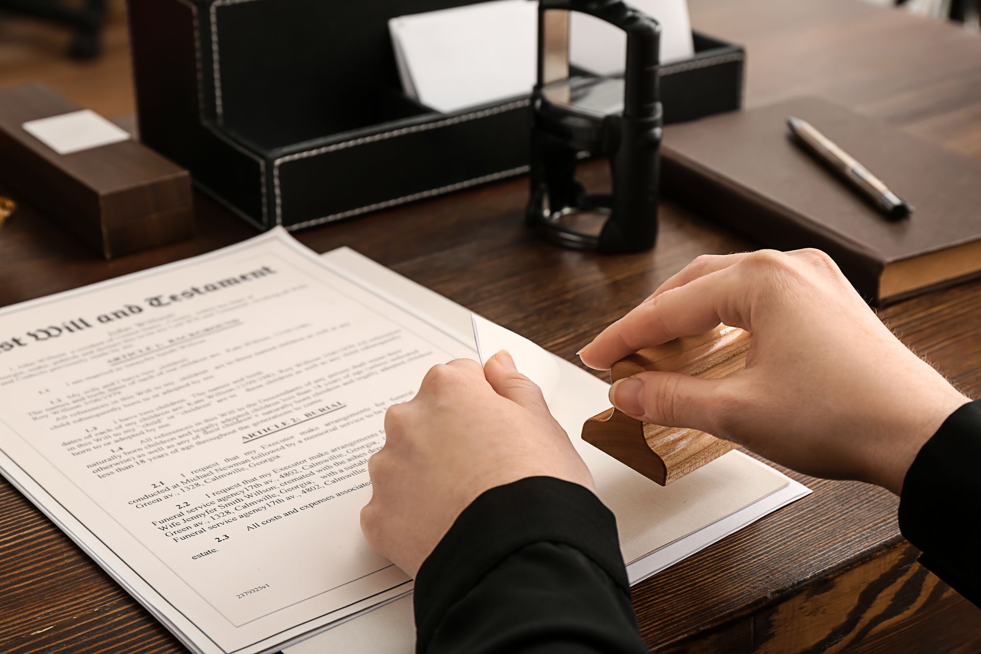 Hands stamping a legal document, possibly a will, on a wooden desk