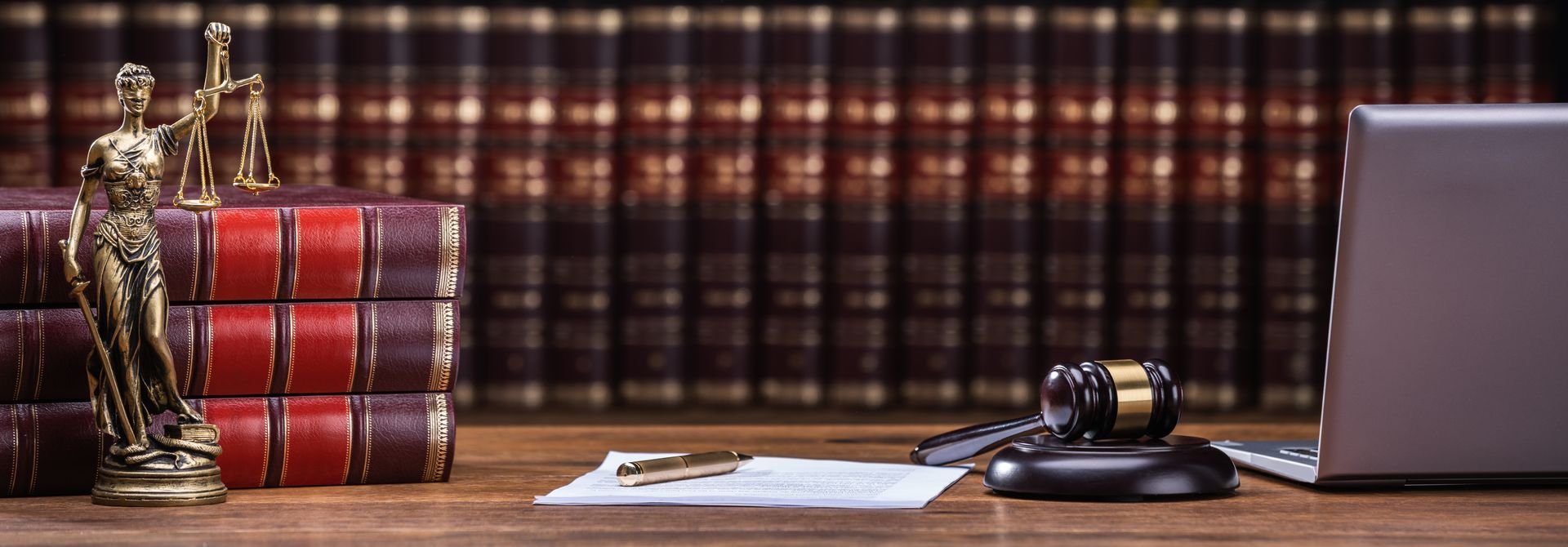 Legal office scene: statue of justice, books, gavel, document, and laptop on wooden desk