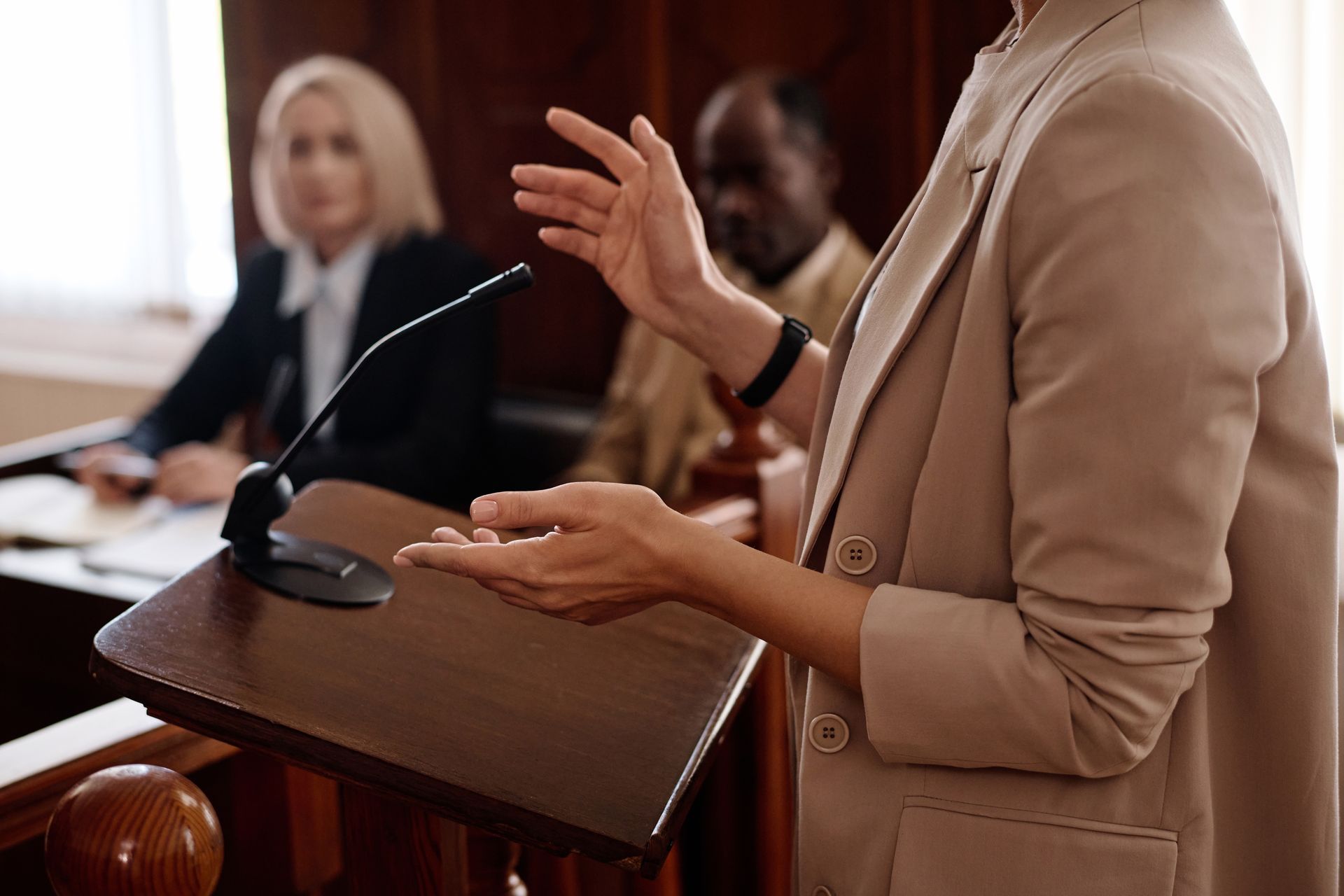 Person speaking at a podium in a courtroom, gesturing with hands