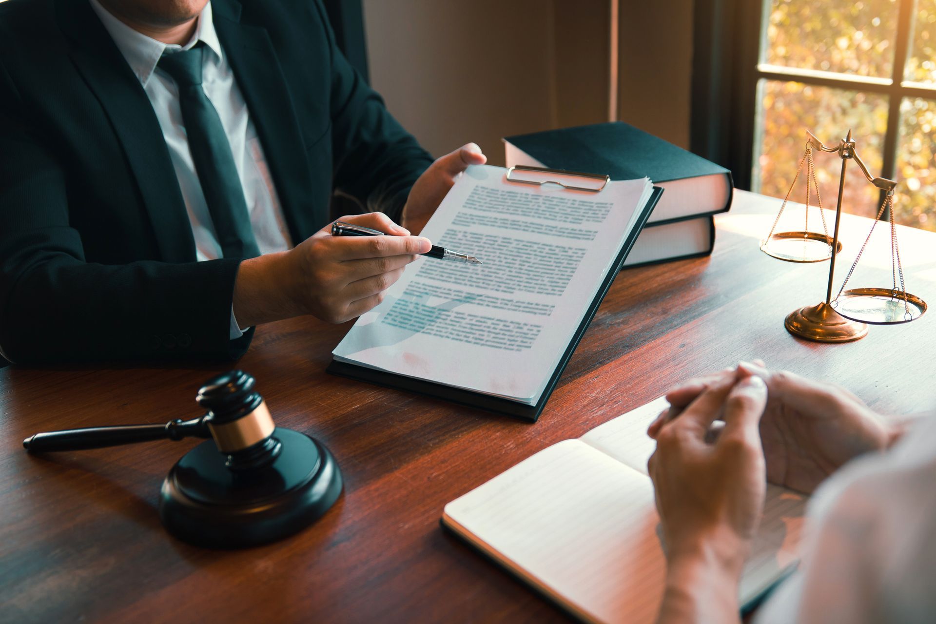 Attorney pointing to a document during a consultation, with a gavel and scales of justice on the table