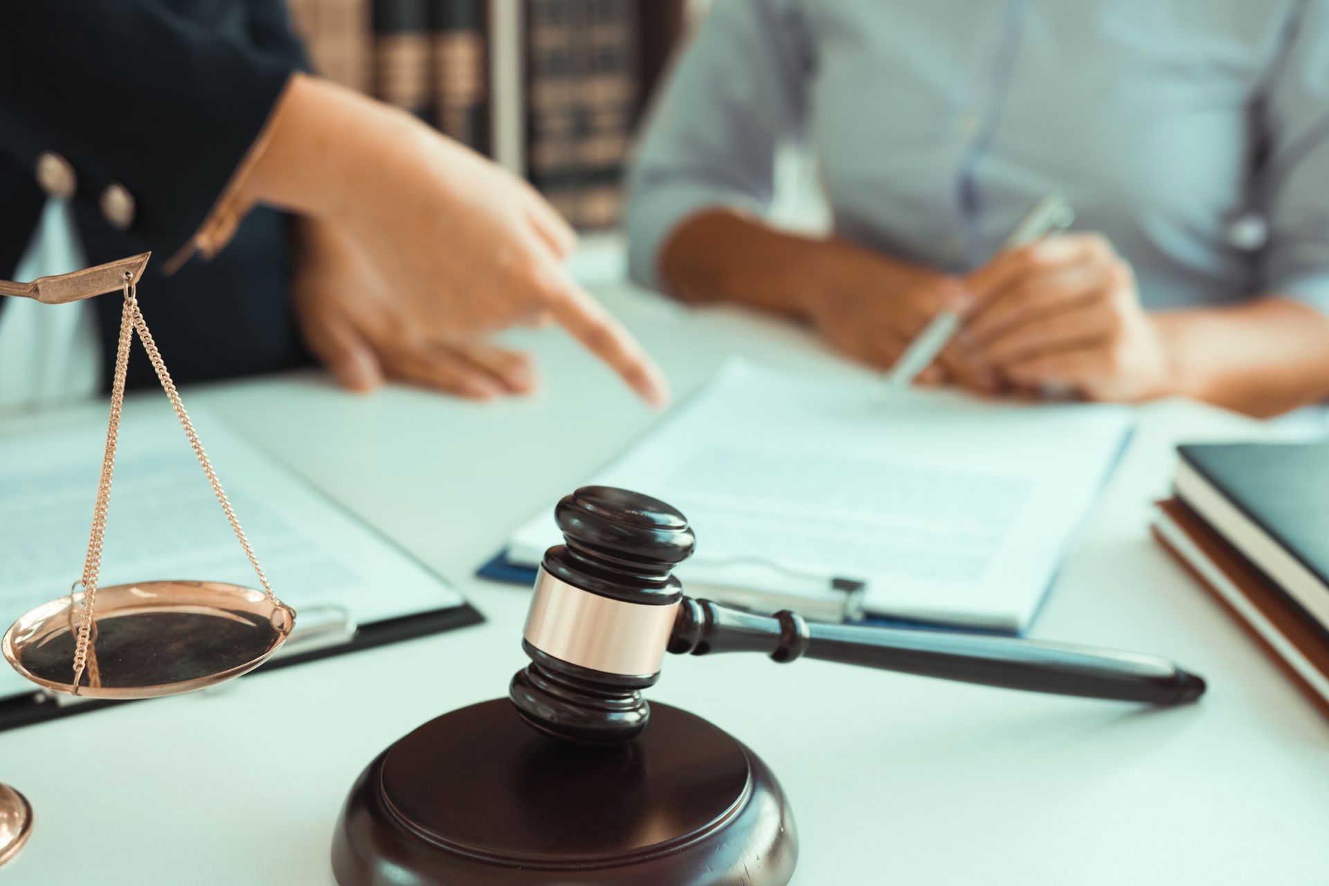 Gavel, scales, documents, and two people reviewing paperwork at a desk. One person points