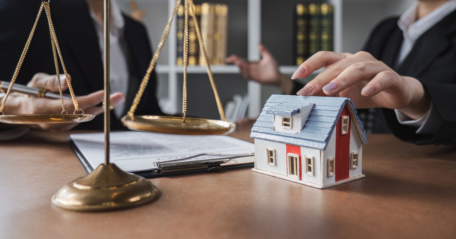 A miniature house and scales of justice on a table with an attorney, discussing property or legal matters
