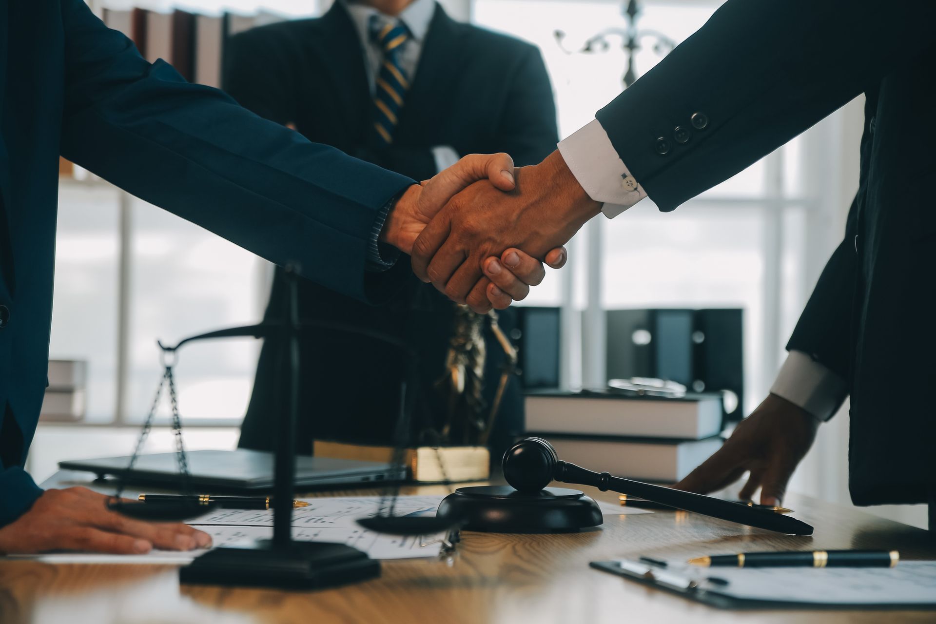 Two business people shaking hands over a desk in a law office, a gavel in view