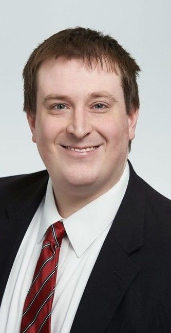 Man in a suit smiles at the camera, red and black striped tie, light background. Man in a suit smiles at the camera, red and black striped tie, light background.