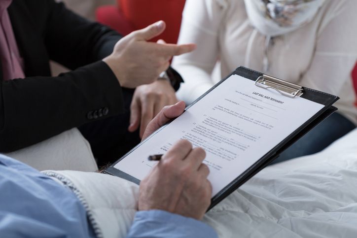 Person in bed signing a document on a clipboard