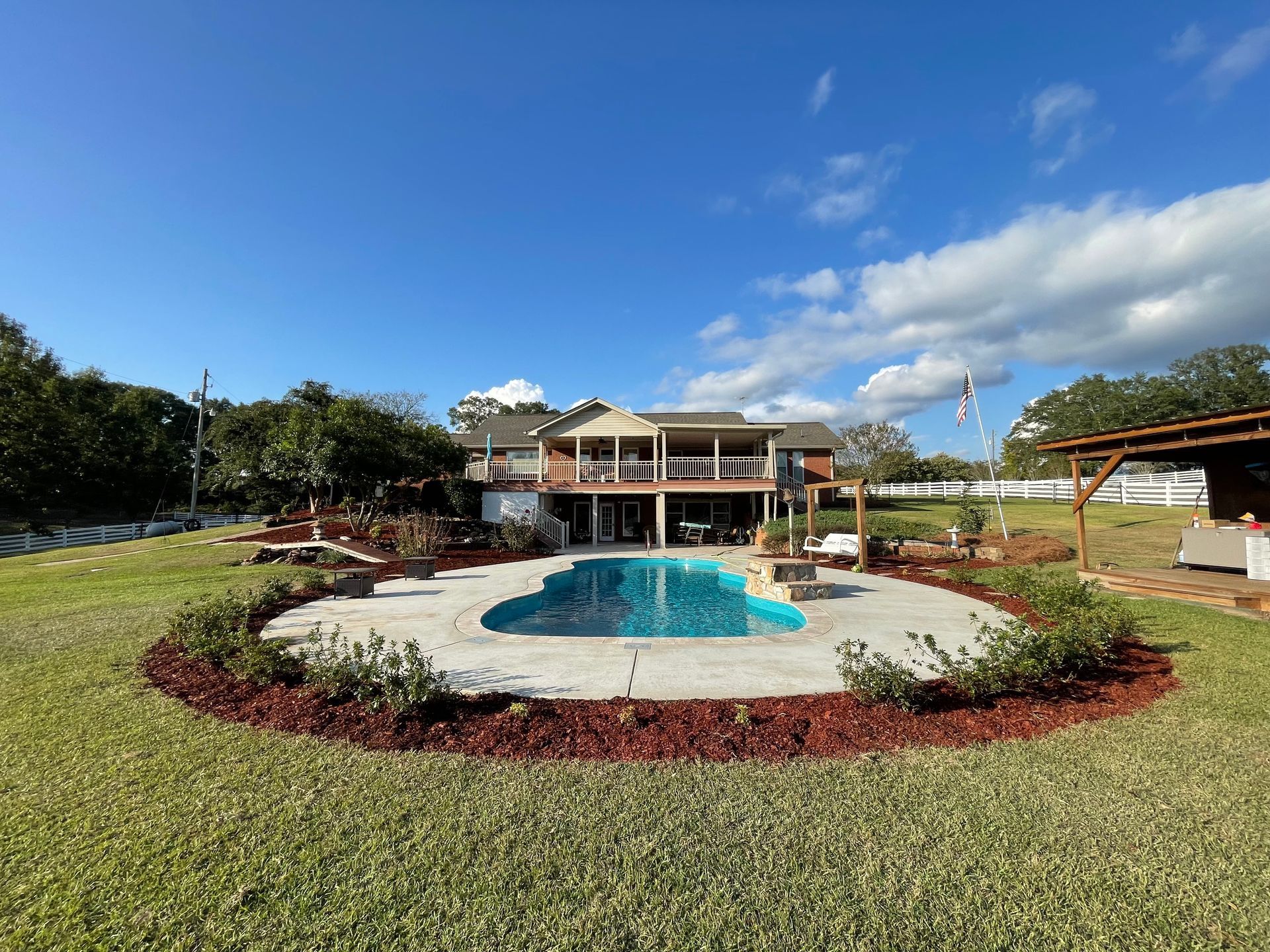 House with swimming pool on a sunny day; lawn with landscaping and blue sky.