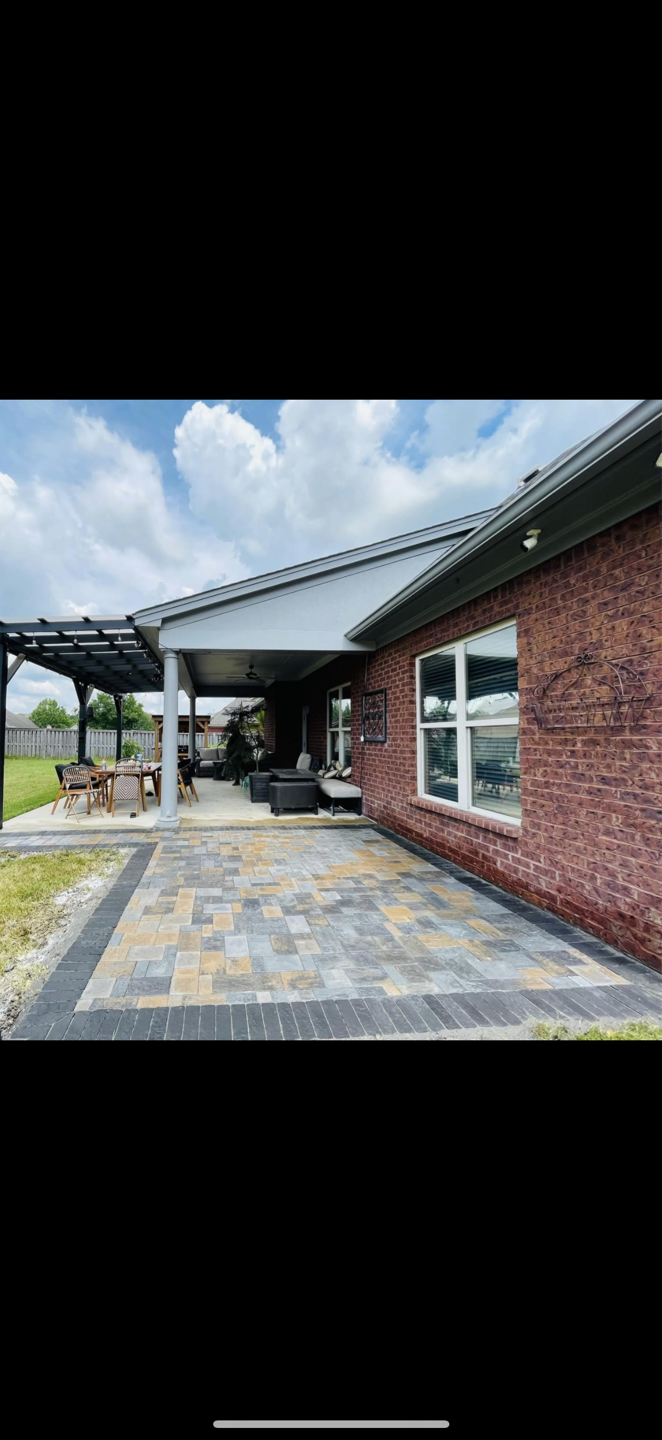 A brick house with a paved patio, covered seating area, and a pergola.
