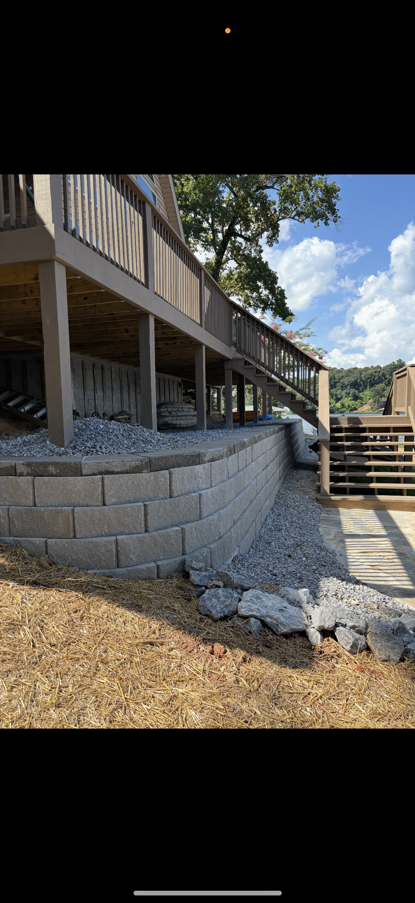 A wooden deck built on pillars, next to a retaining wall of gray blocks, and gravel.